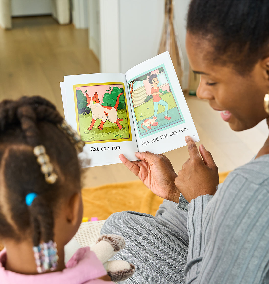 An adult reads a children's book with a young child. The open pages show illustrated scenes with the captions Cat can run and Min and Cat can run.